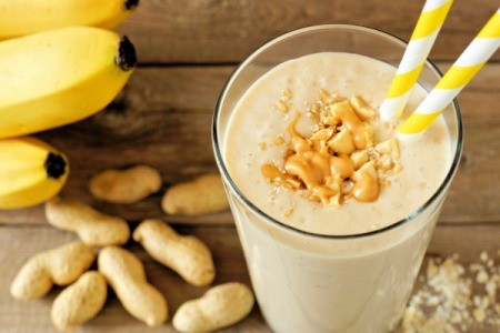 A smoothie in a glass with peanuts and bananas around.