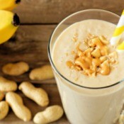 A smoothie in a glass with peanuts and bananas around.