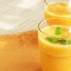 Two orange colored smoothies in glasses.