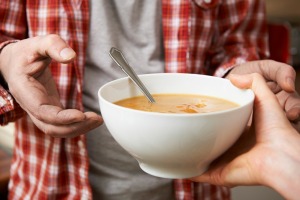 A bowl of soup being handed to a hungry person.