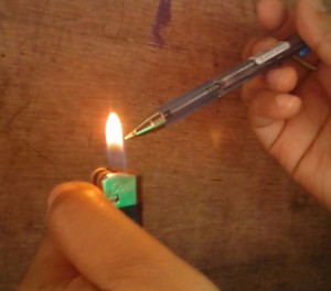 A ballpoint pen being heated in the flame of a pocket lighter.