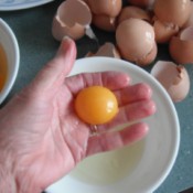 An egg yolk in a hand, with the egg white is caught in a bowl underneath.