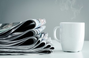 A stack of newspaper next to a cup of coffee.