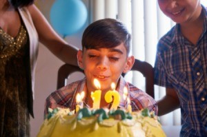 A birthday cake with a "12" on the top and a boy blowing out the candles.