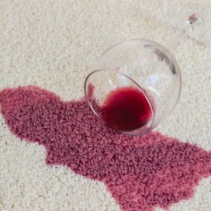 A glass of red wine spilled on a light colored carpet.