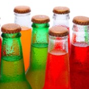 A bunch of brightly colored sodas in clear glass bottles.
