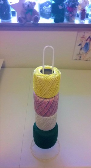 Several rolls of crochet thread on a toilet paper holder.