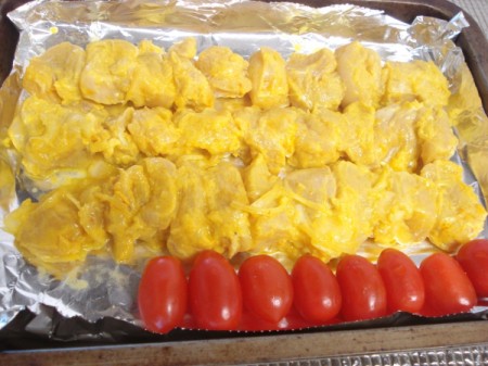 chicken on skewers and tomatoes on foil lined pan ready to cook
