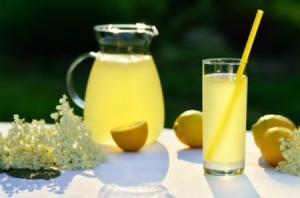 A pitcher and glass of lemonade on a table outside.