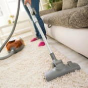 A woman cleaning a carpet in front of a door and couch.