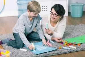 Babysitter handing a 7 year old, who is coloring, a piece of chalk.