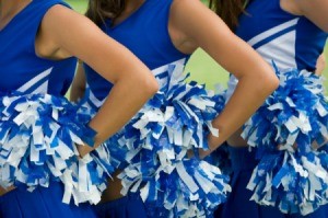 Closeup of 3 cheerleaders arms on hips holding pom poms.