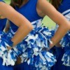 Closeup of 3 cheerleaders arms on hips holding pom poms.