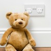 Teddybear sitting next to a childproofed outlet.