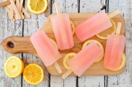 Pink popsicles on a wooded cutting board with slices of lemon.