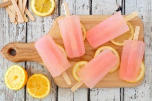 Pink popsicles on a wooded cutting board with slices of lemon.
