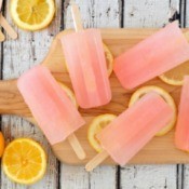 Pink popsicles on a wooded cutting board with slices of lemon.