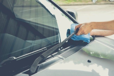 A person cleaning a windshield with a blue cloth.