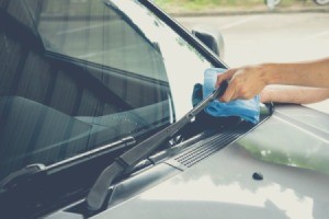 A person cleaning a windshield with a blue cloth.