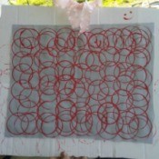 Fabric Stamp Art - white fabric with red overlapping paint circles mounted to a piece of cardboard