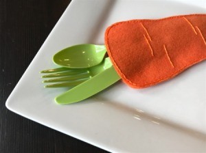 Felt Carrot Utensil Holder - green plasticware protruding from carrot pocket onto corner of plate