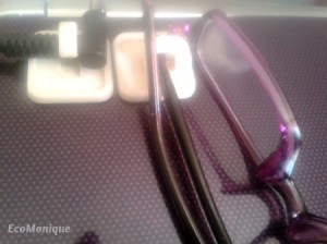 Cords and eyeglasses hanging on Command hooks on the side of a laptop.
