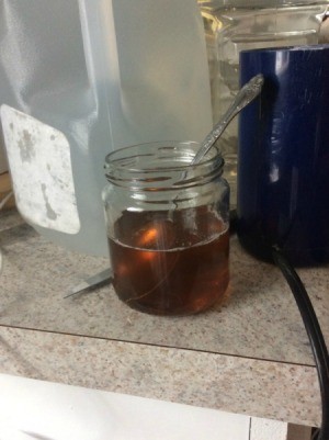 A metal spoon inside a glass jar full of hot liquid.