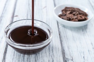 Someone pouring chocolate syrup in a small glass bowl.