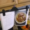 A pants hanger being used to display a cookbook in the kitchen.