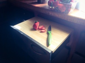 A cutting board placed on top of an open drawer in the kitchen.