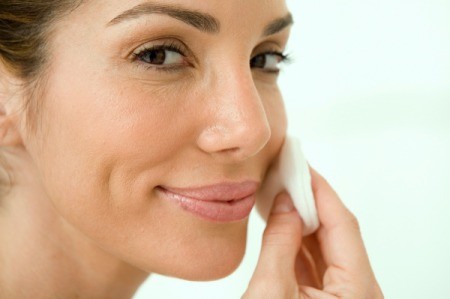 A smiling woman cleaning her face.