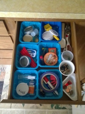 An organized junk drawer using recycled containers as dividers.