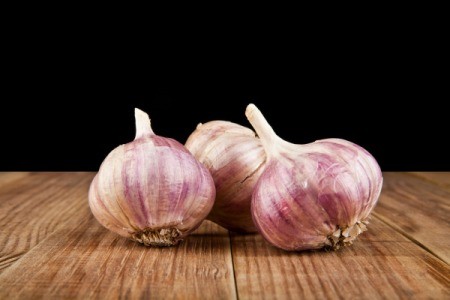 Three heads of garlic on a wooden surface.