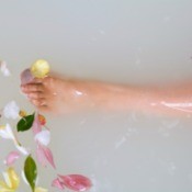 A lower leg in a bathtub, filled with milk and flowers.