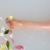 A lower leg in a bathtub, filled with milk and flowers.