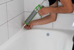 A person caulking around a bathtub.