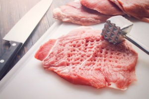 A cut of meat and a metal meat tenderizer.