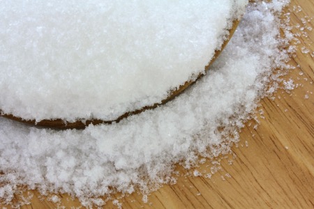 A bowl of epsom salts, spilling onto a wooden surface.