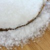 A bowl of epsom salts, spilling onto a wooden surface.