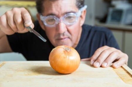 A man wearing swimming goggles while cutting an onion.