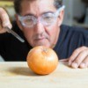 A man wearing swimming goggles while cutting an onion.