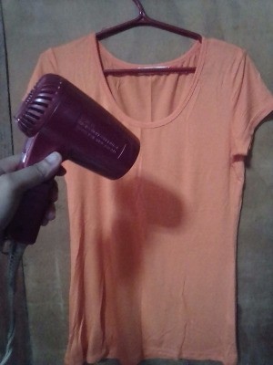 A hair dryer being used to remove wrinkles from a shirt.