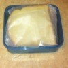 A sandwich wrapped in wax paper and then stored in a plastic container.