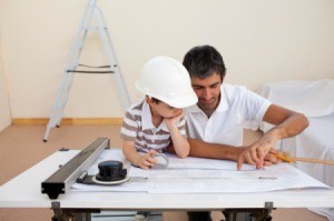 A boy at work with his father, looking at blueprints.