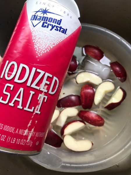 A container of salt next to cut apples in water.