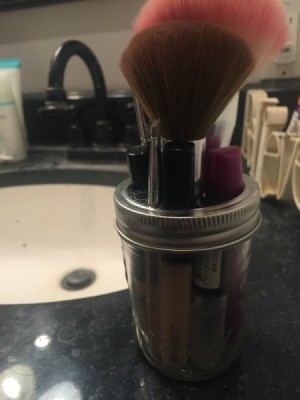 A mason jar with several makeup brushes stored inside.