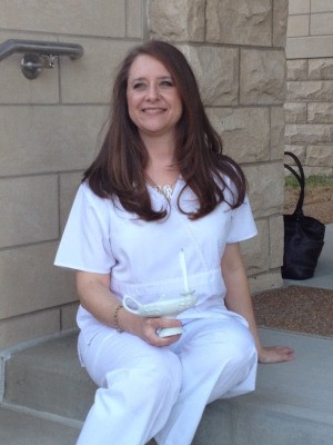 A woman wearing white nursing scrubs and a charm bracelet at her graduation from nursing school.