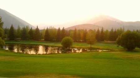 A grassy field with a lake and mountains in the distance.