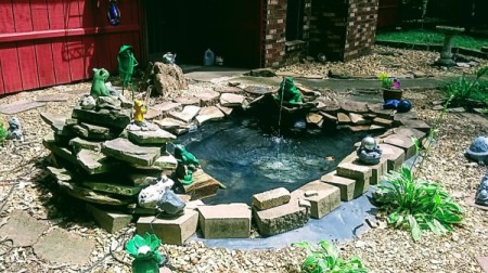 A garden rock pond with decorative frogs all around.