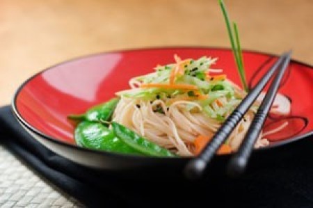 Rice noodles in a red bowl toped with veggies.